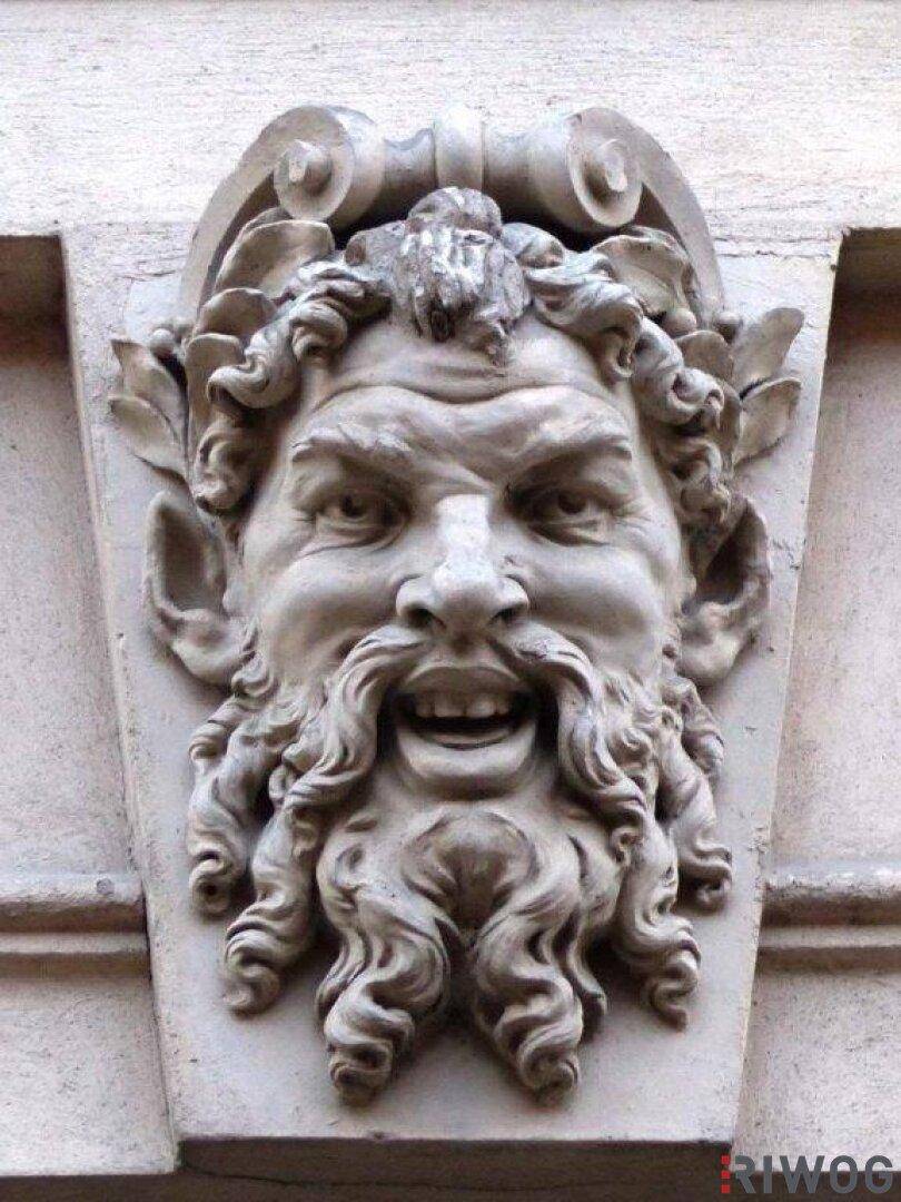 Nahaufnahme einer kunstvollen steinernen Maskaron-Verzierung an der historischen Gebäudefassade.