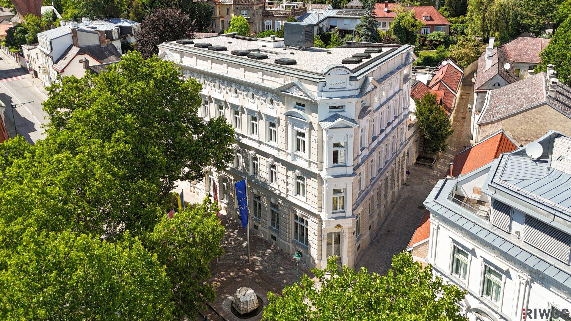Luftaufnahme des historischen Gebäudes mit umliegenden Bäumen und Gebäuden an einem sonnigen Tag.