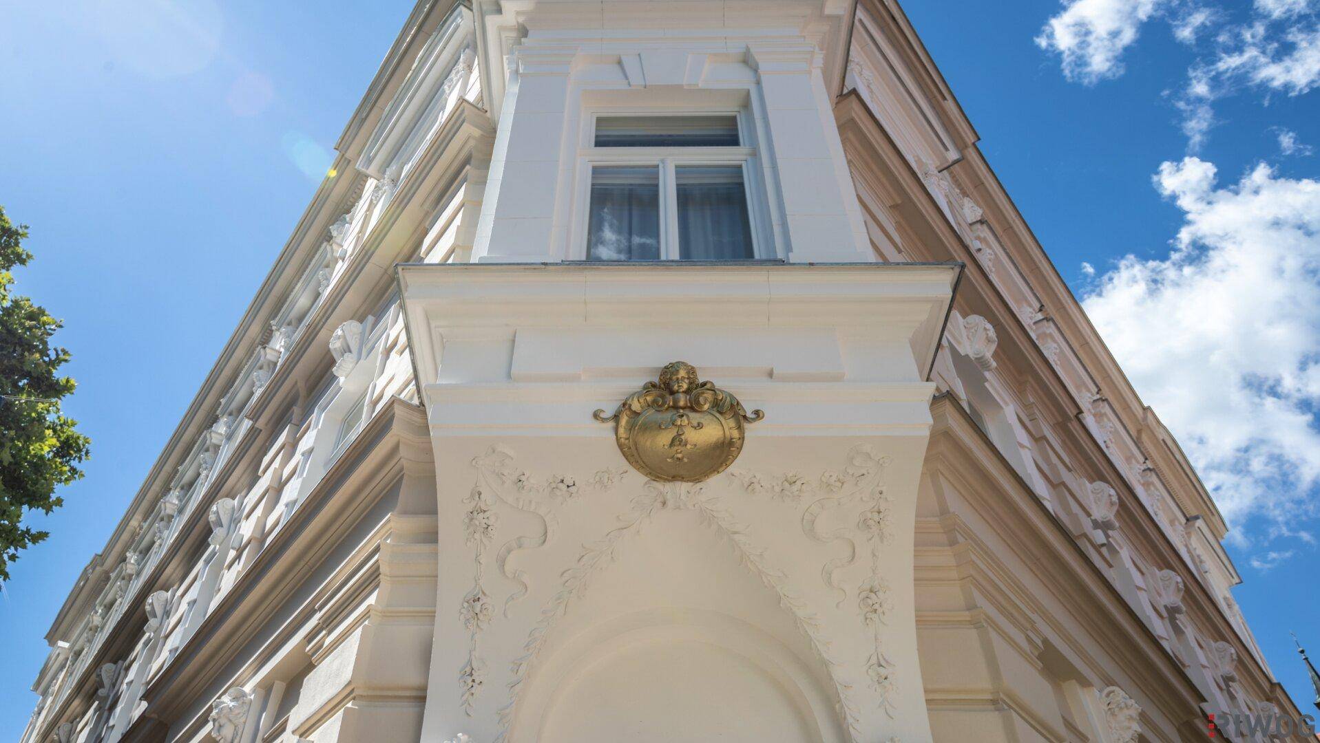 Nahaufnahme eines kunstvollen goldenen Emblems an der historischen Fassade des Gebäudes bei Sonnenschein.