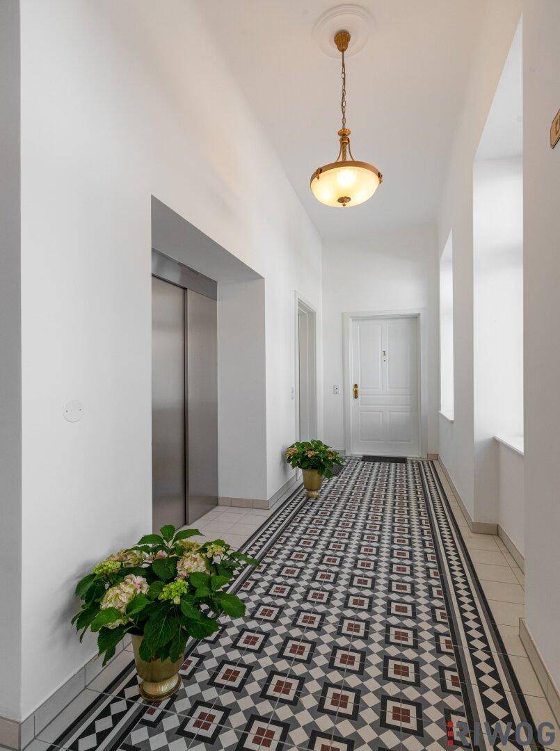 Heller Flur mit elegantem Fliesenboden, Aufzug und einer Eingangstür, geschmückt mit Pflanzen.