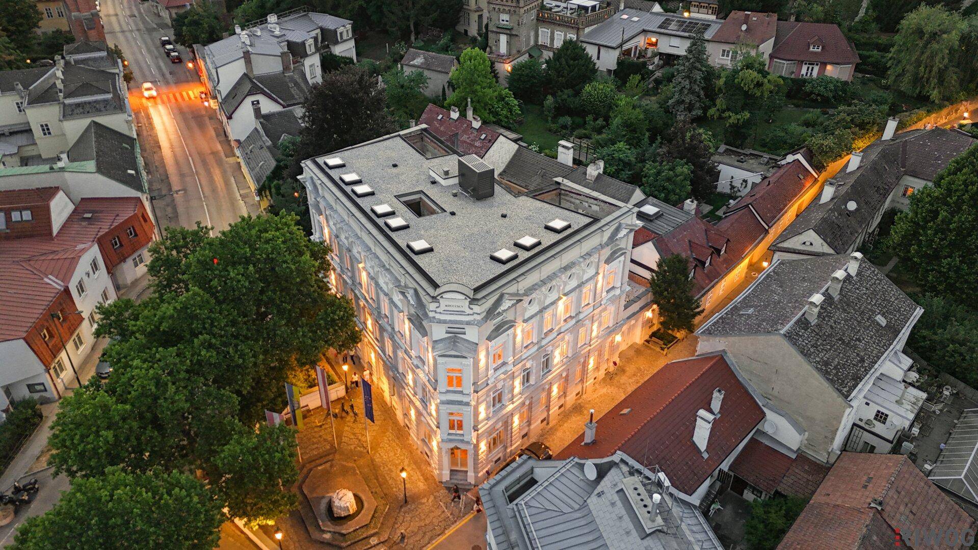 Abendliche Luftaufnahme des beleuchteten Gebäudes, umgeben von einer ruhigen Stadtstraße.
