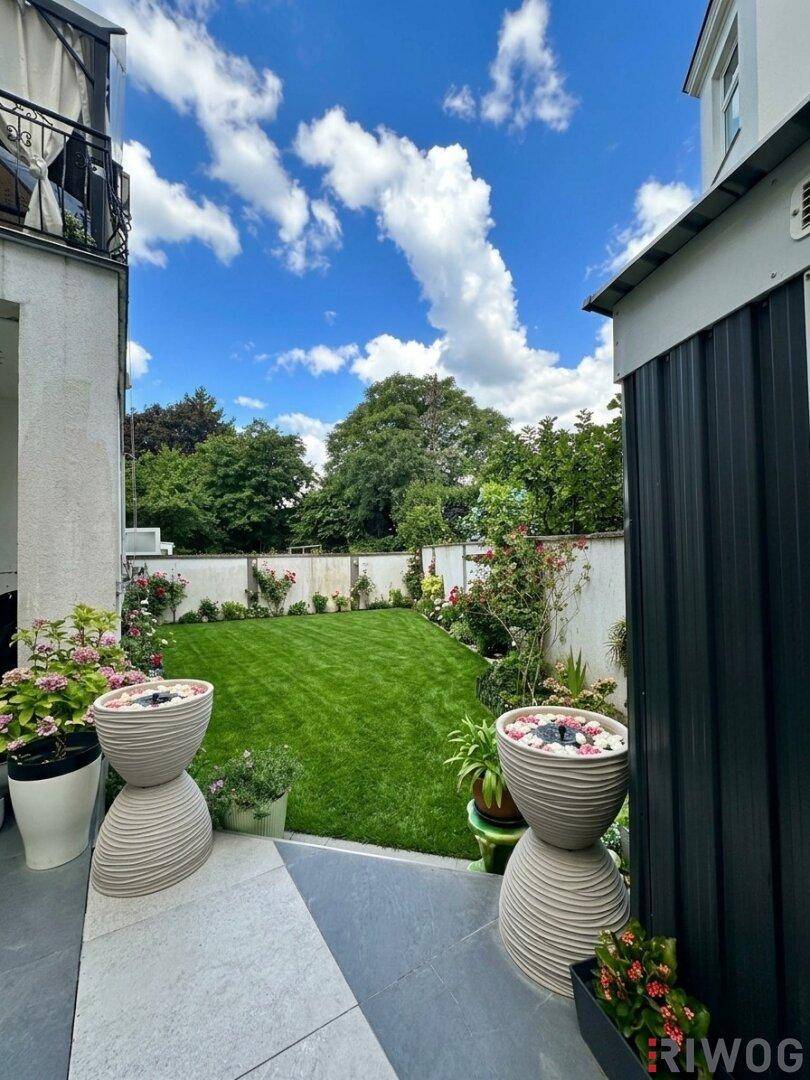 Gepflegter Gartenbereich mit Rasenfläche, Blumenbeeten und moderner Terrassenfliesen.