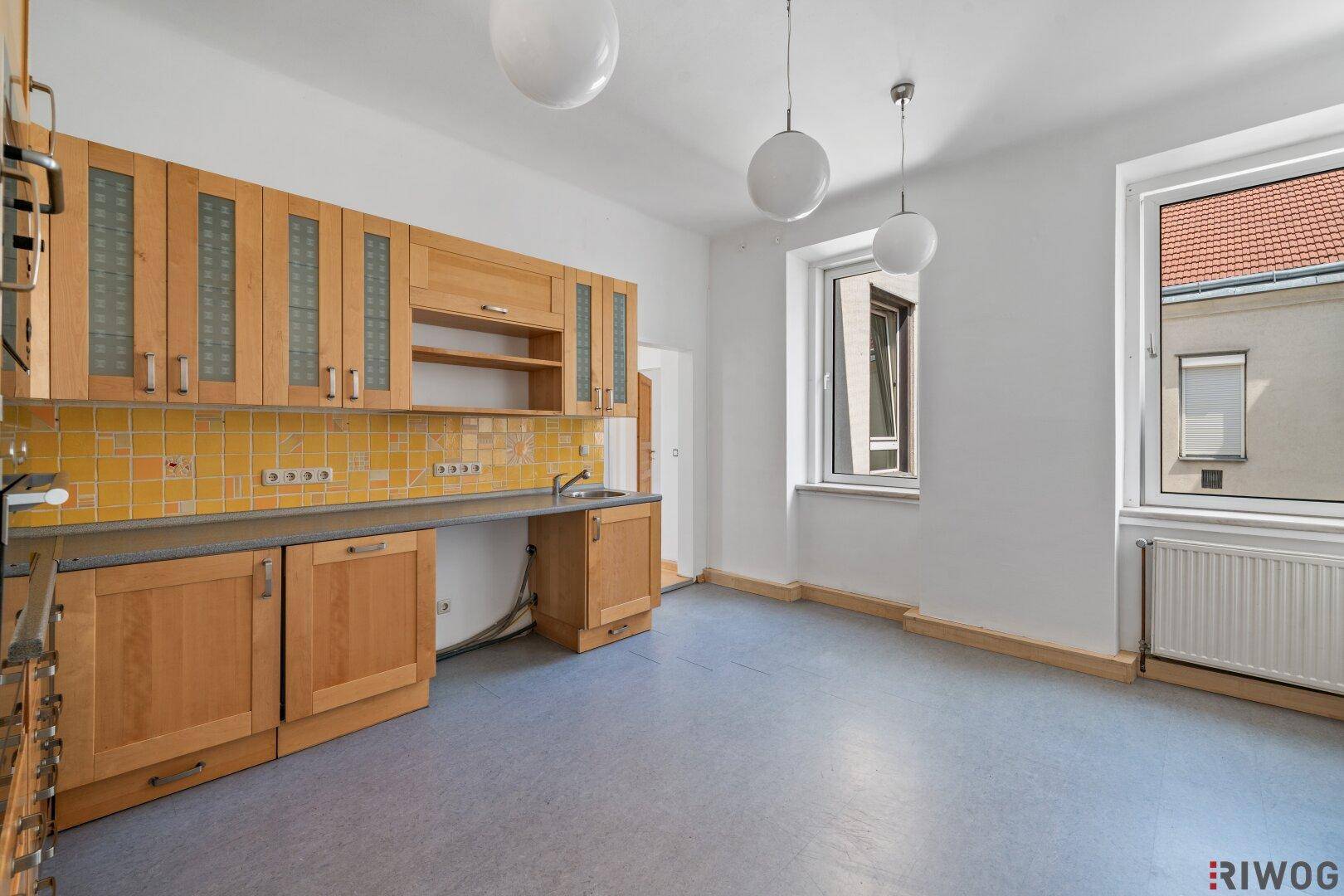 Helle Küche mit Holzschränken, gelben Fliesen und zwei Fenstern für viel Tageslicht.