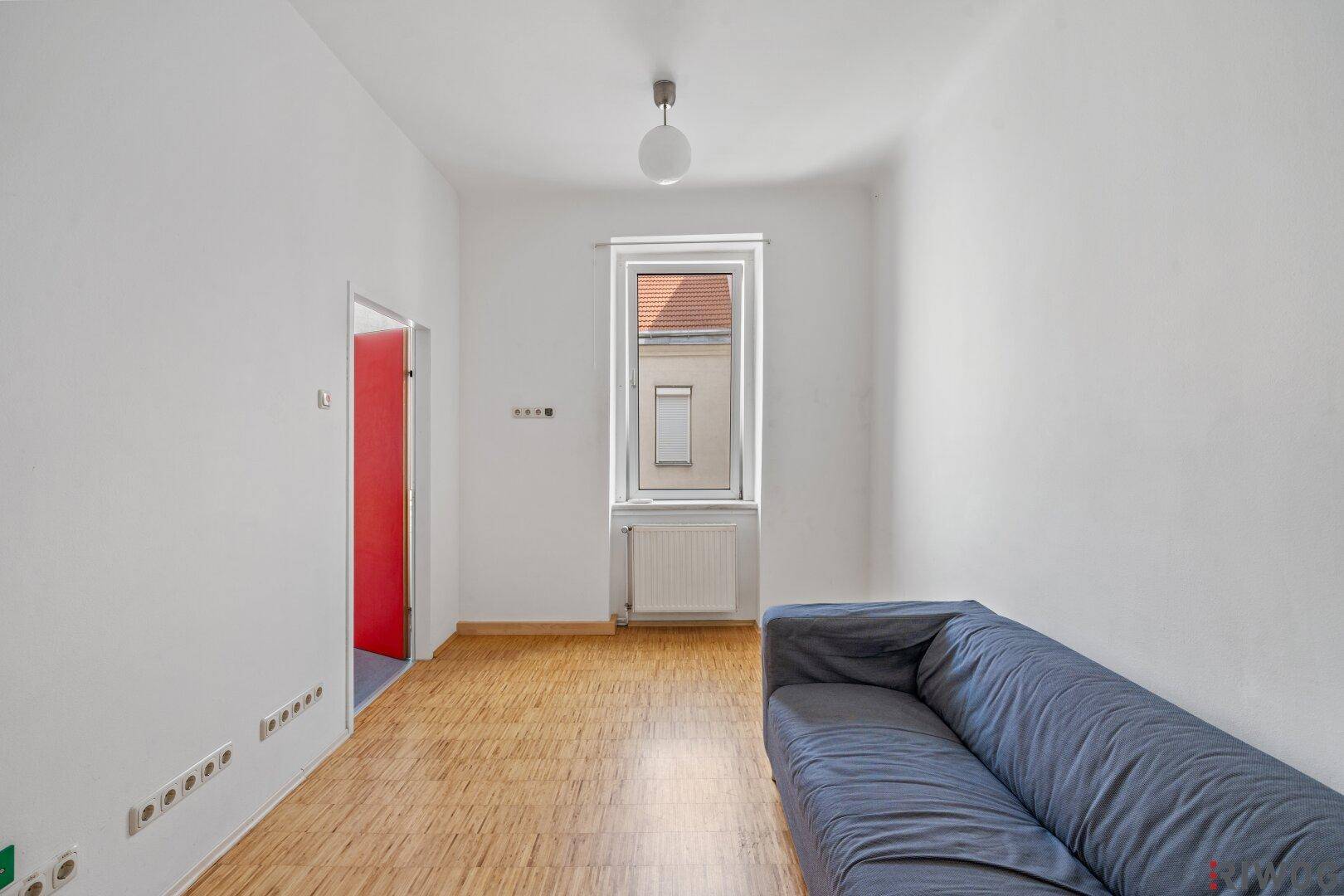 Helles Wohnzimmer mit Holzboden und einem Fenster, das viel Tageslicht hereinlässt.