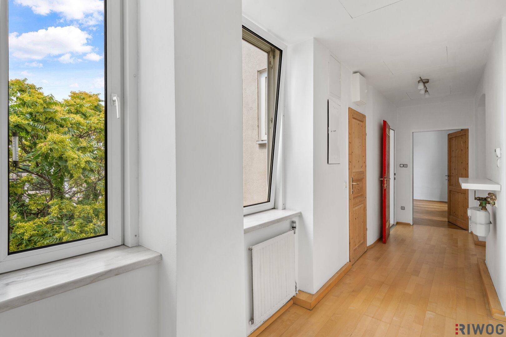 Heller Flur mit Holzboden und einem Fenster, das einen Blick ins Grüne bietet.