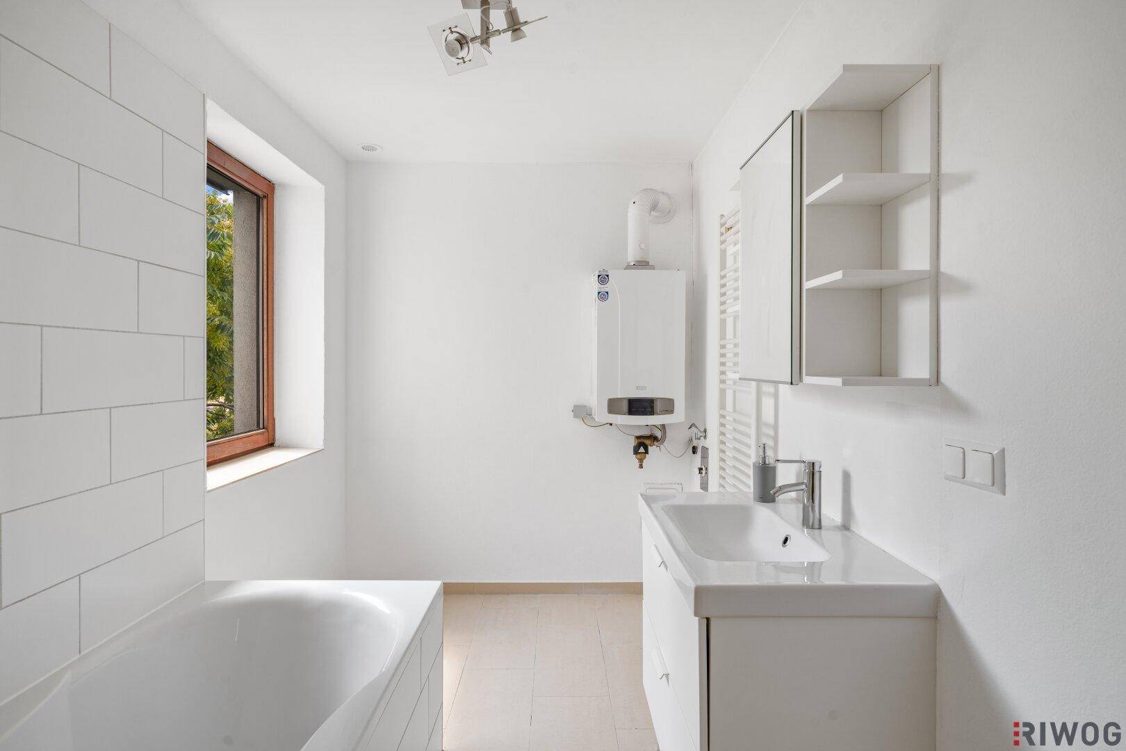 Modernes Badezimmer mit Badewanne, Waschbecken und Fenster, hell gefliest.