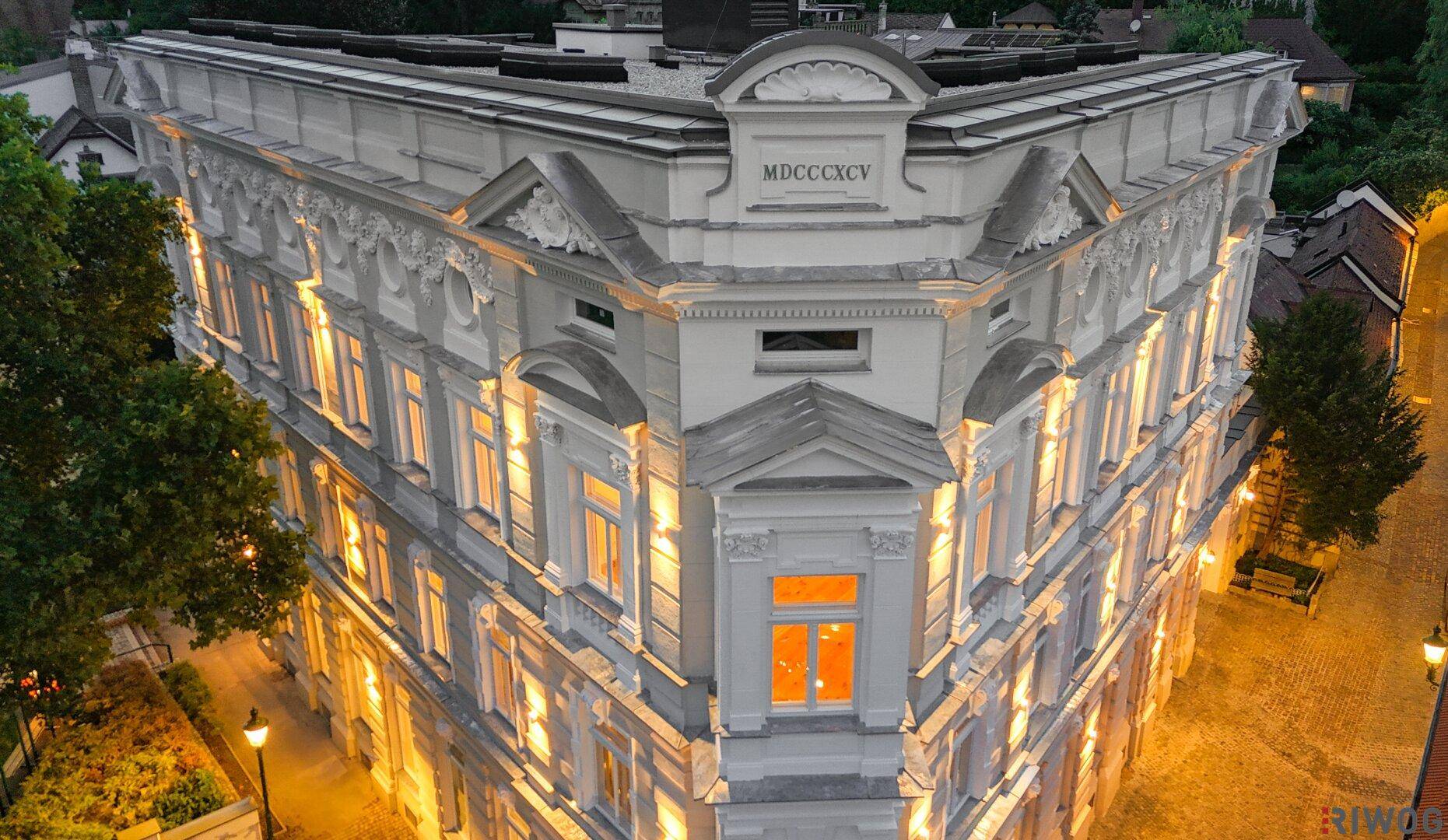 Beleuchtetes Eckgebäude bei Nacht mit historischen Details und der Jahreszahl MDCCCXCV.