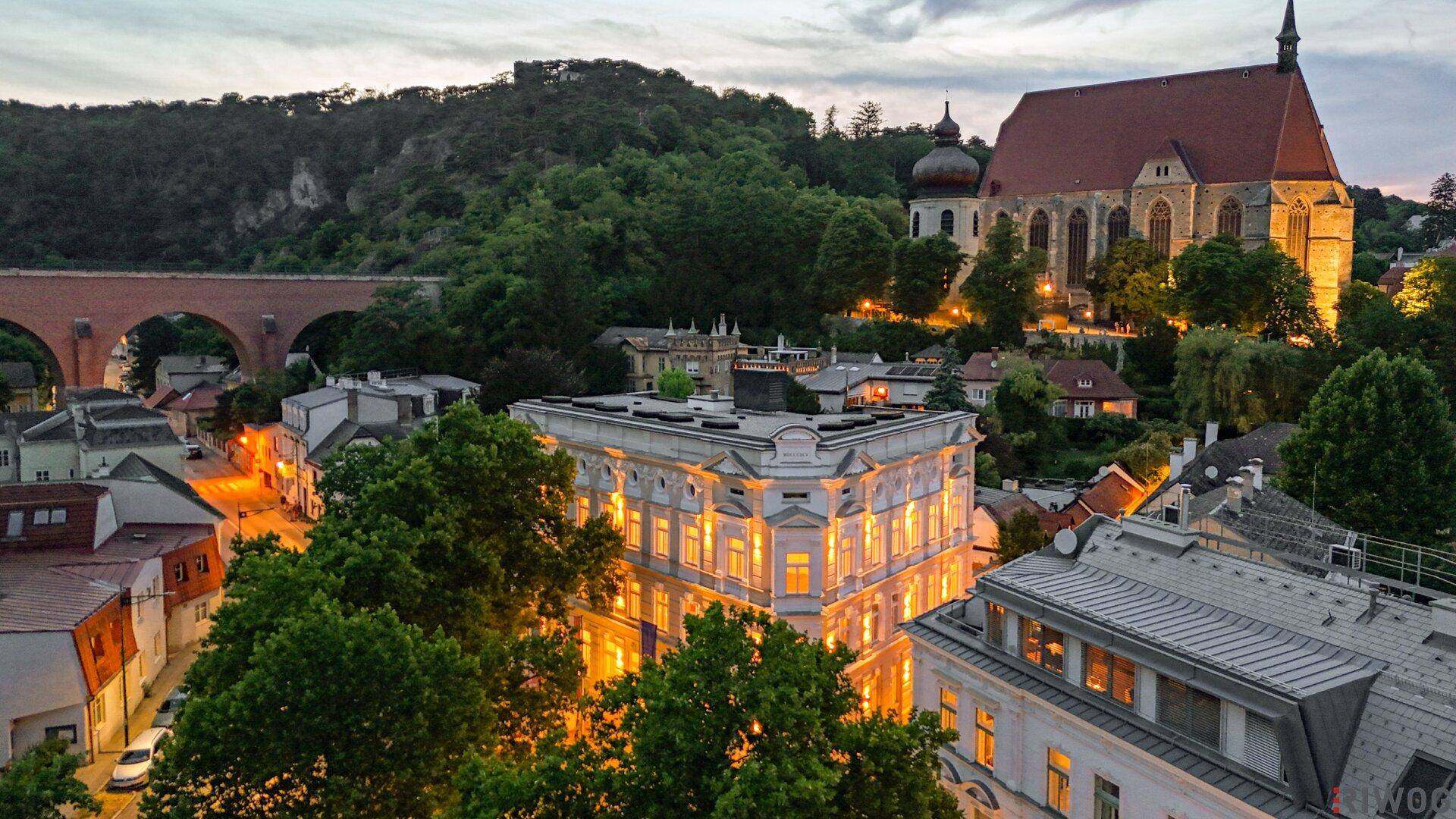 Panoramablick auf das beleuchtete Gebäude und die historische Stadtkulisse bei Dämmerung.