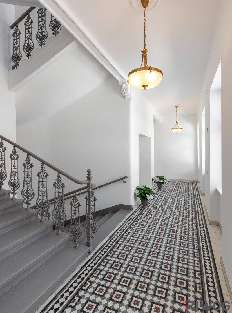 Eleganter Flur mit kunstvollem Treppengeländer, gemustertem Fliesenboden und hohen Decken im Altbau.