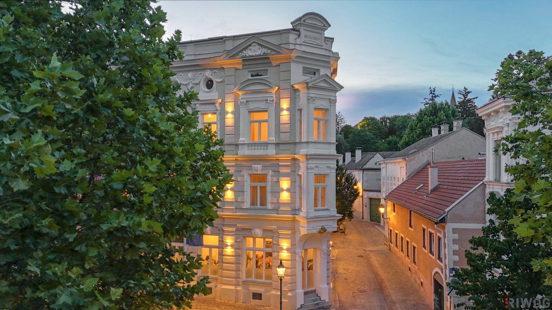 Beleuchtetes Eckgebäude mit eleganter Architektur und großen Fenstern bei Abenddämmerung.
