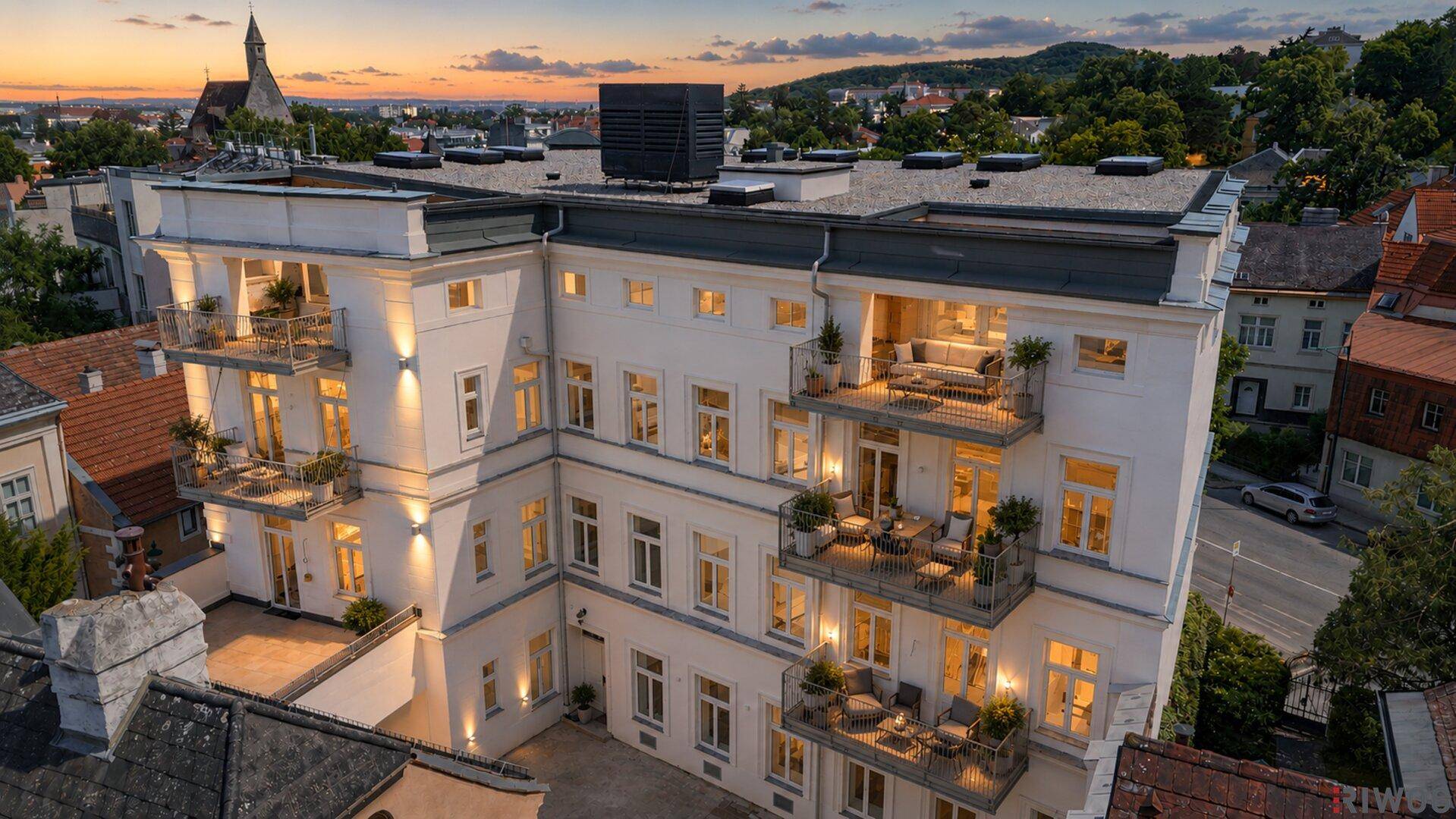 Abendliche Luftaufnahme des Gebäudes mit beleuchteten Balkonen und Blick auf die Stadt.