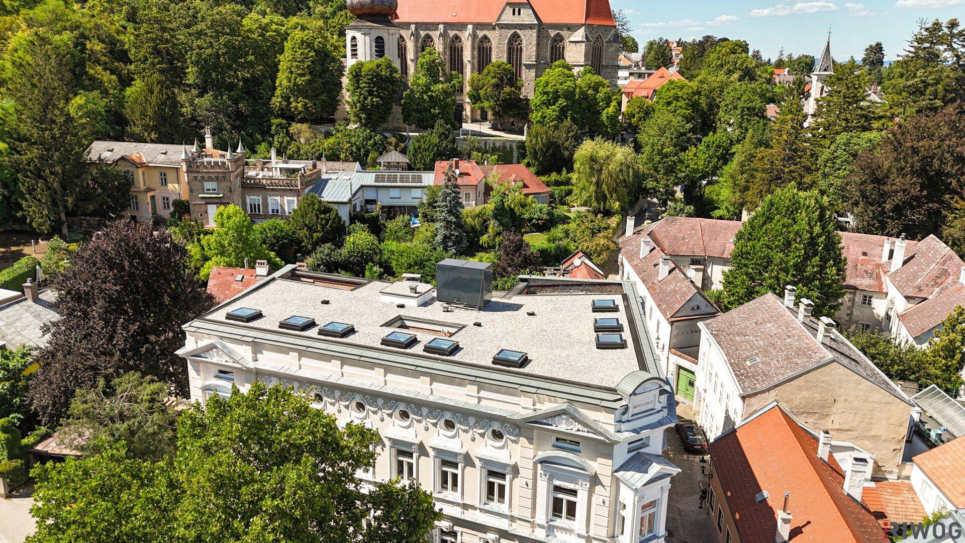 Luftaufnahme des historischen Gebäudes mit Flachdach und umliegender grüner Landschaft.