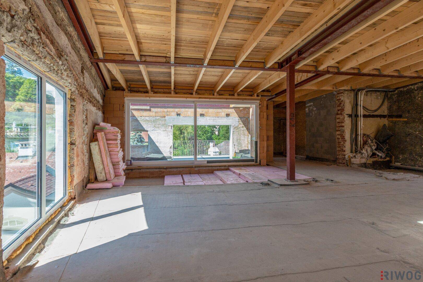 Großer Innenraum im Rohbau mit hohen Decken und großen Fensterfronten, bereit für den Ausbau.
