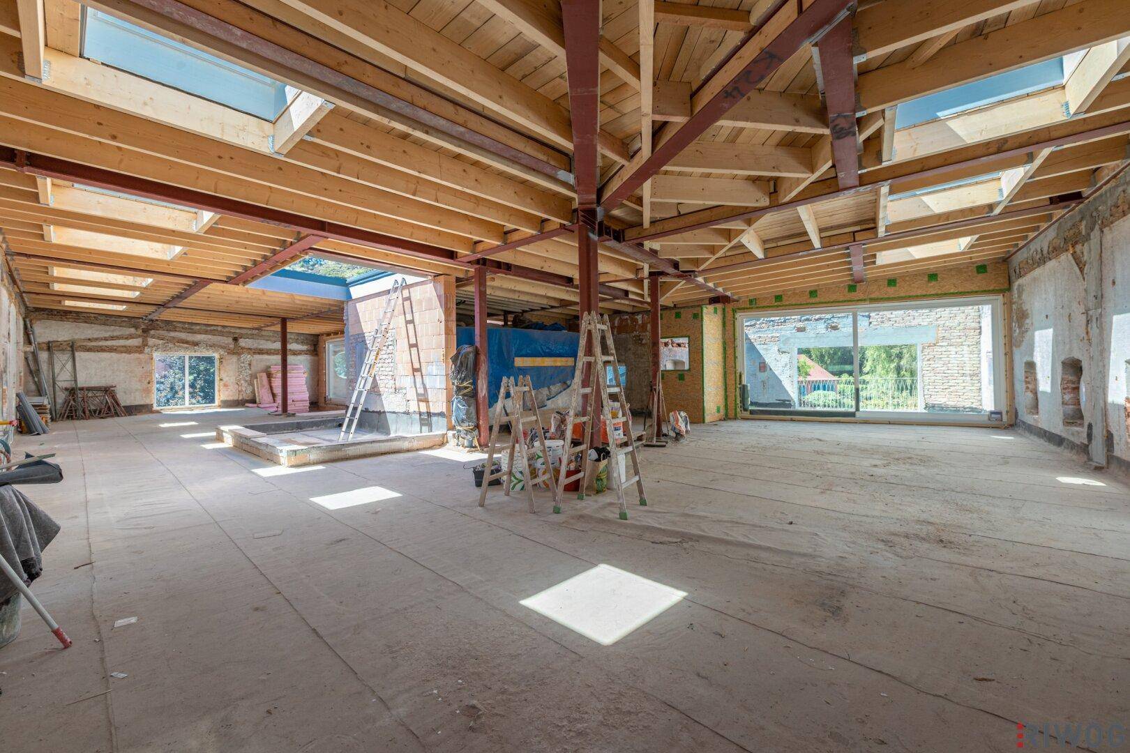 Großer offener Innenraum im Rohbau mit sichtbaren Holzbalken und Dachfenstern.