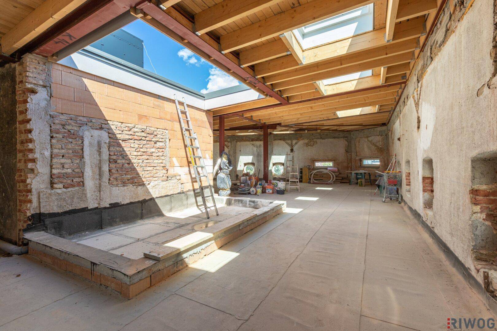 Geräumiger Rohbau mit Holzbalken, Dachfenstern und einer zukünftigen Terrasse im Freien.