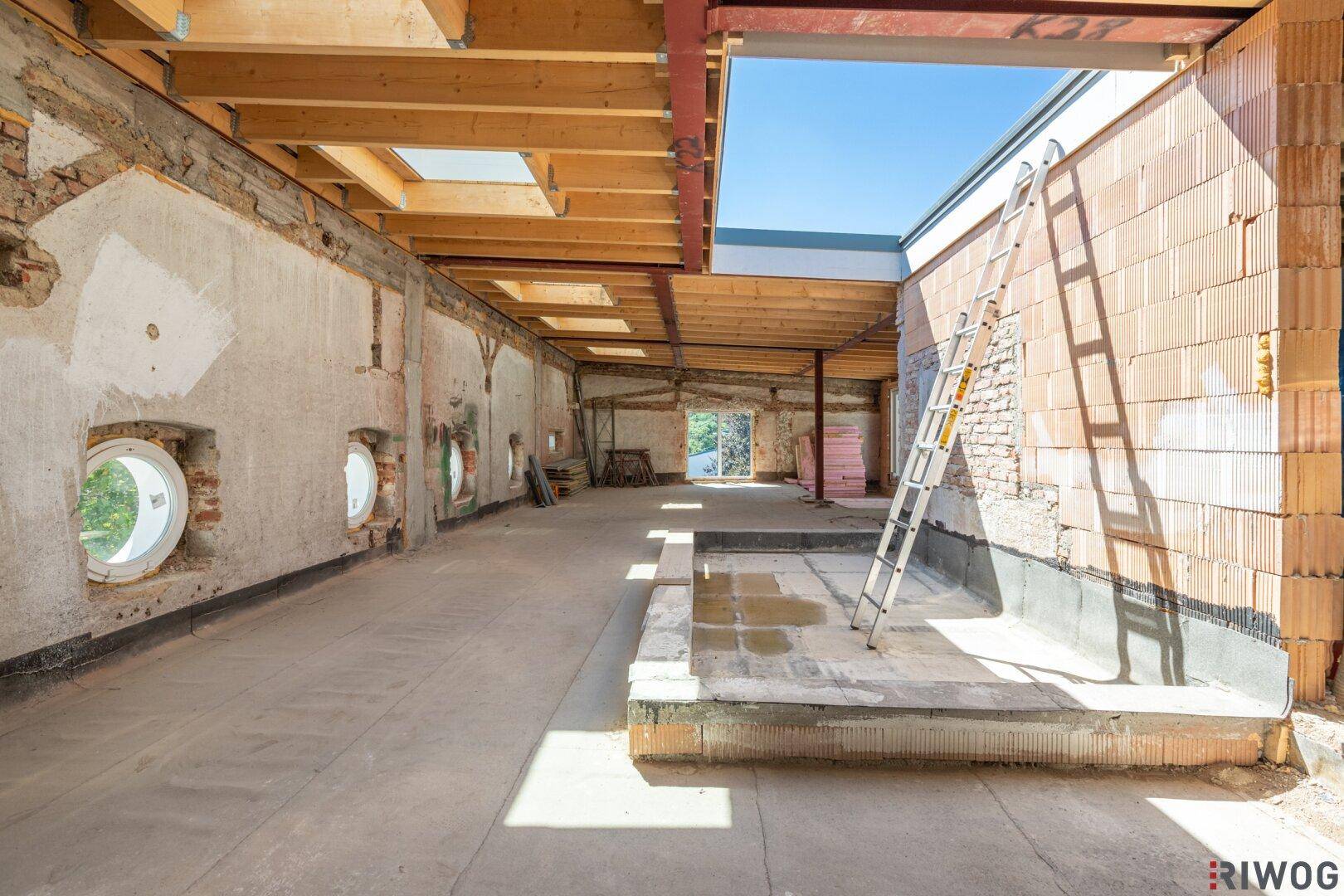 Heller Rohbau mit Holzbalkendecke, Ziegelwänden und einem großen Dachfenster für viel Licht.