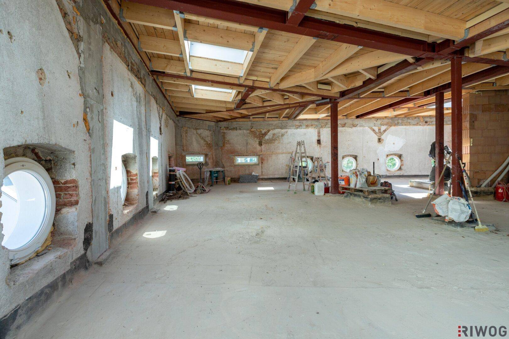 Offener Rohbau mit Holzbalkendecke, runden Fenstern und viel Tageslicht für zukünftige Wohnräume.