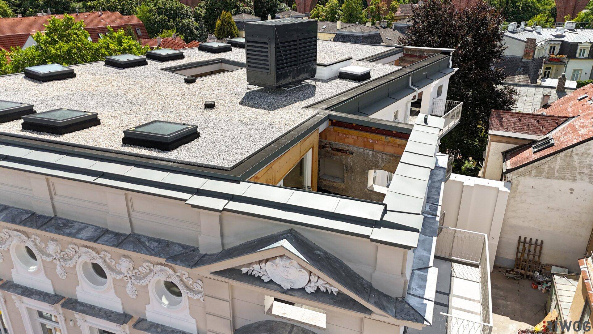 Detailansicht der verzierten Fassade und des Flachdachs mit Kiesbelag und Lüftungsschacht.