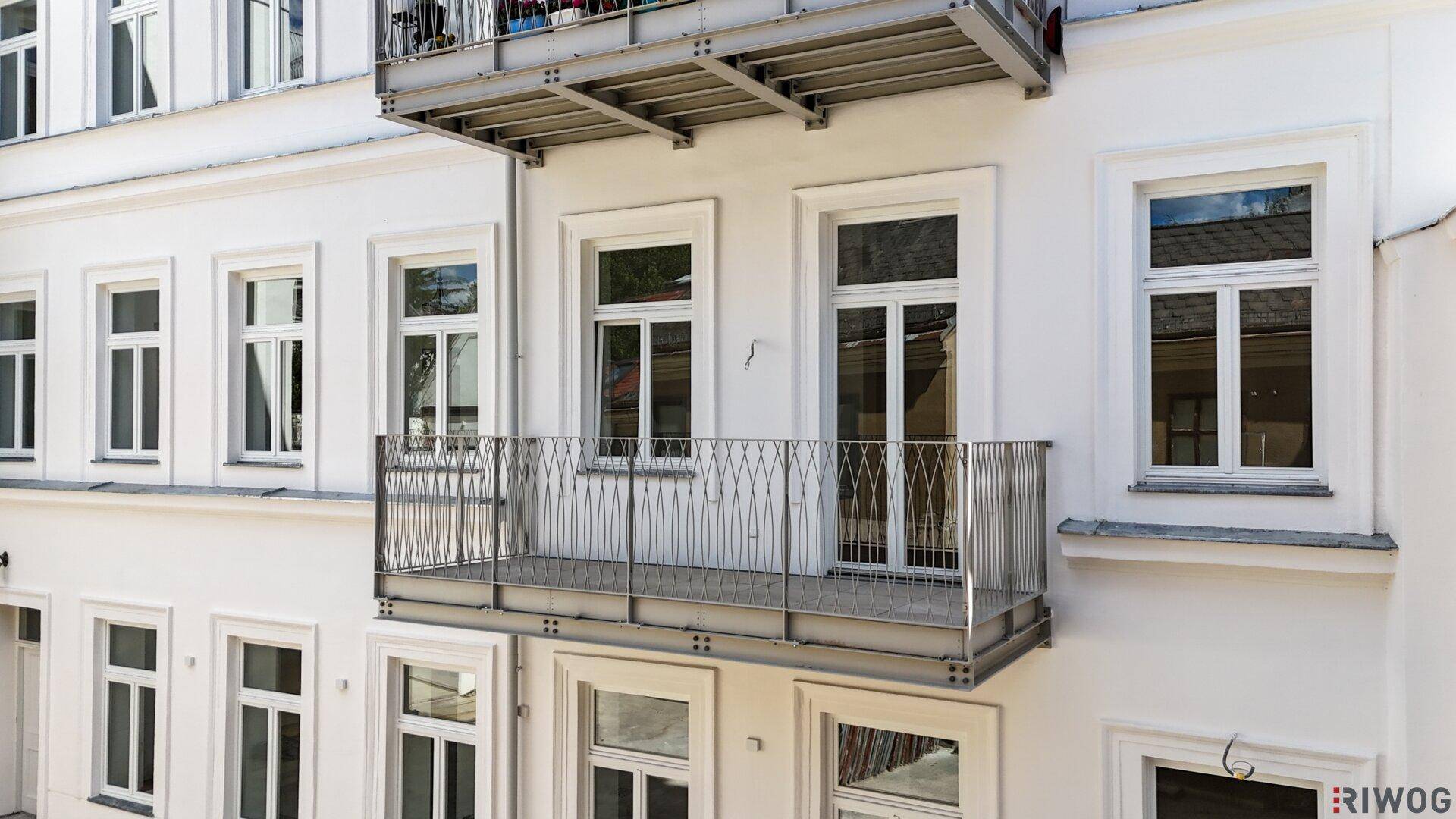 Unmöblierter Balkon mit Metallgeländer an einer weißen Gebäudefassade.