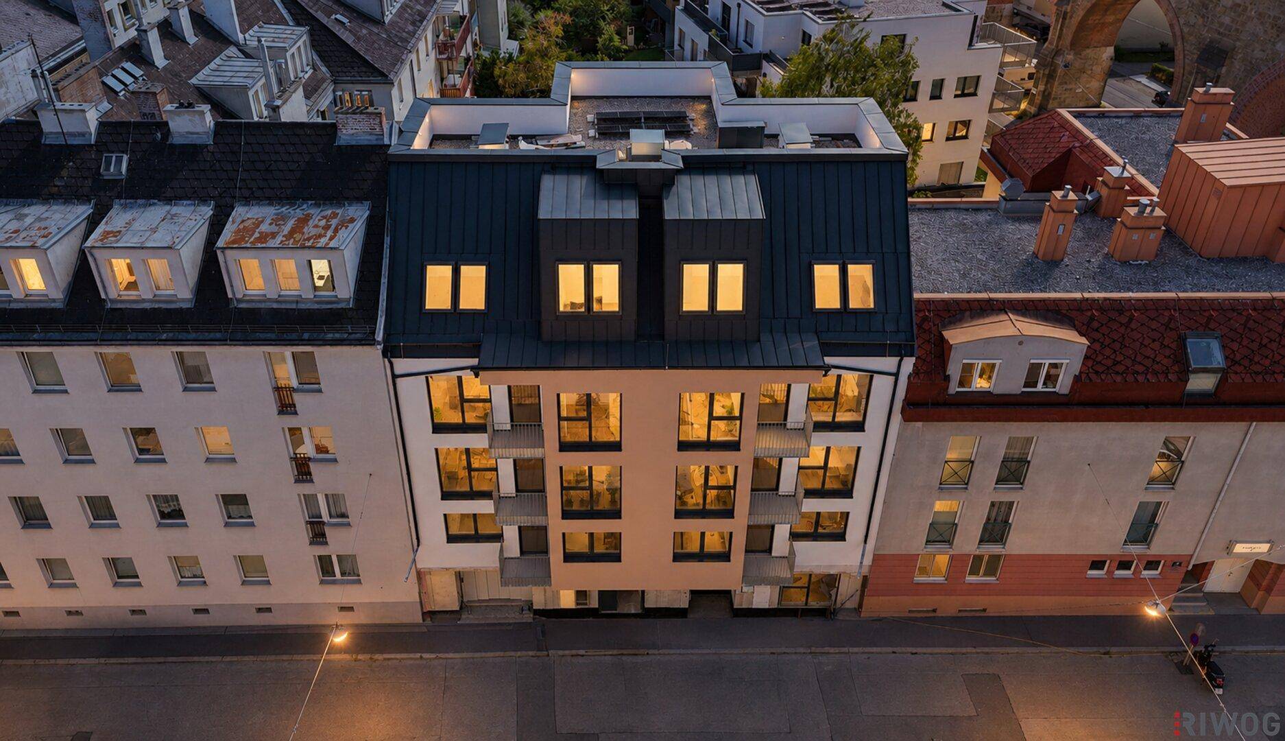 Fassade des modernen Apartmentgebäudes bei Nacht mit beleuchteten Fenstern und Dachgeschosswohnungen.