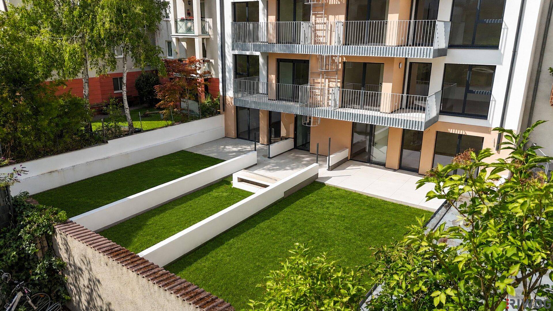Private Gärten und Terrassen im Erdgeschoss des modernen Apartmentgebäudes mit gepflegtem Rasen.