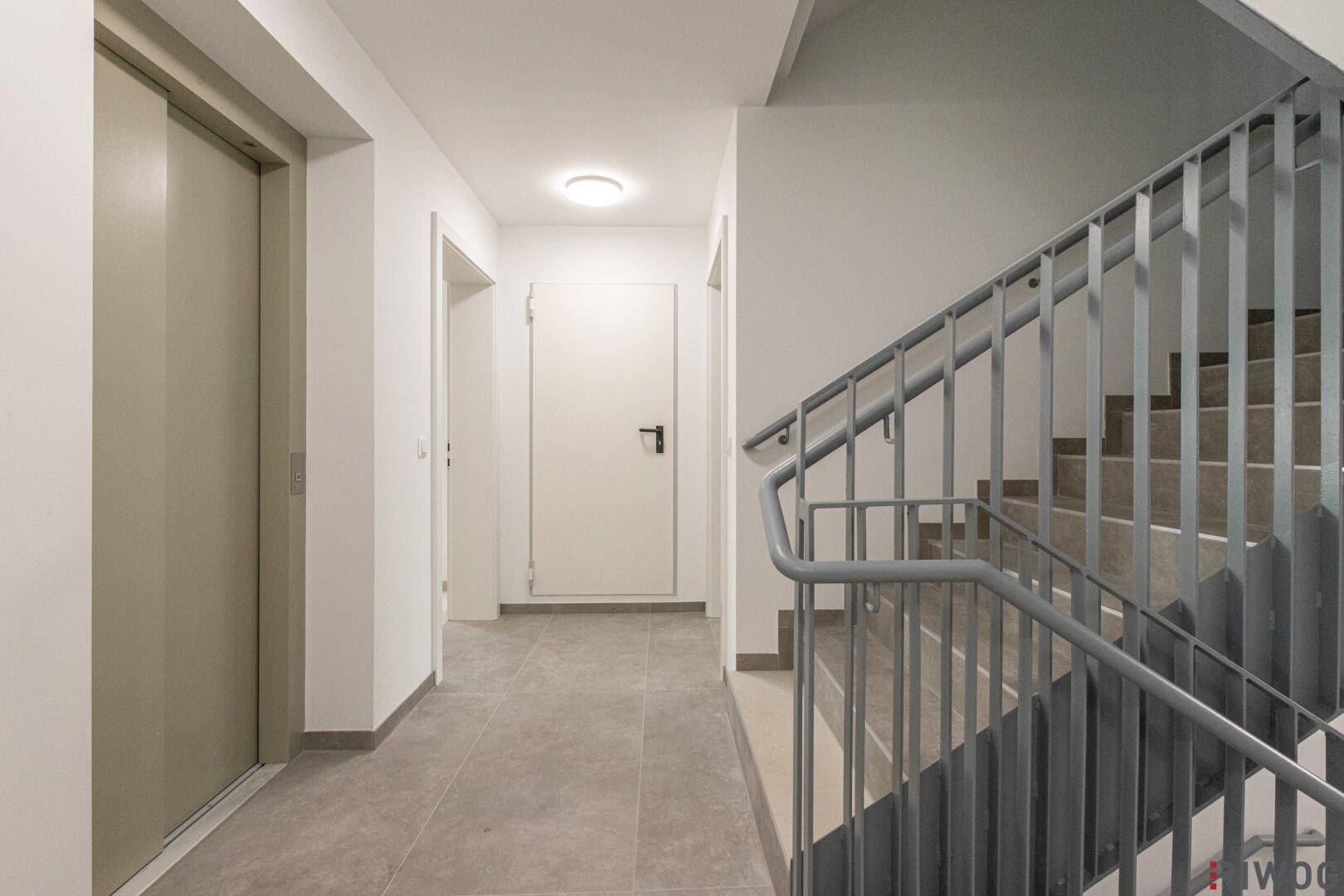 Treppenhaus und Aufzug in einem modernen Gebäude mit Fliesenboden.