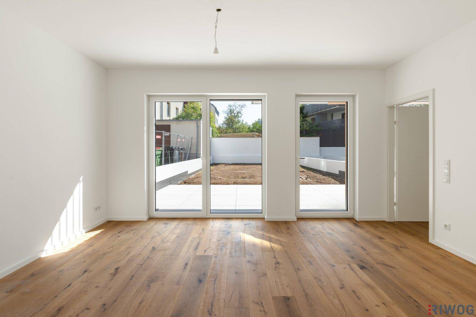 Helles, leeres Wohnzimmer mit Eichenparkettboden und großen Schiebetüren zum Gartenbereich.