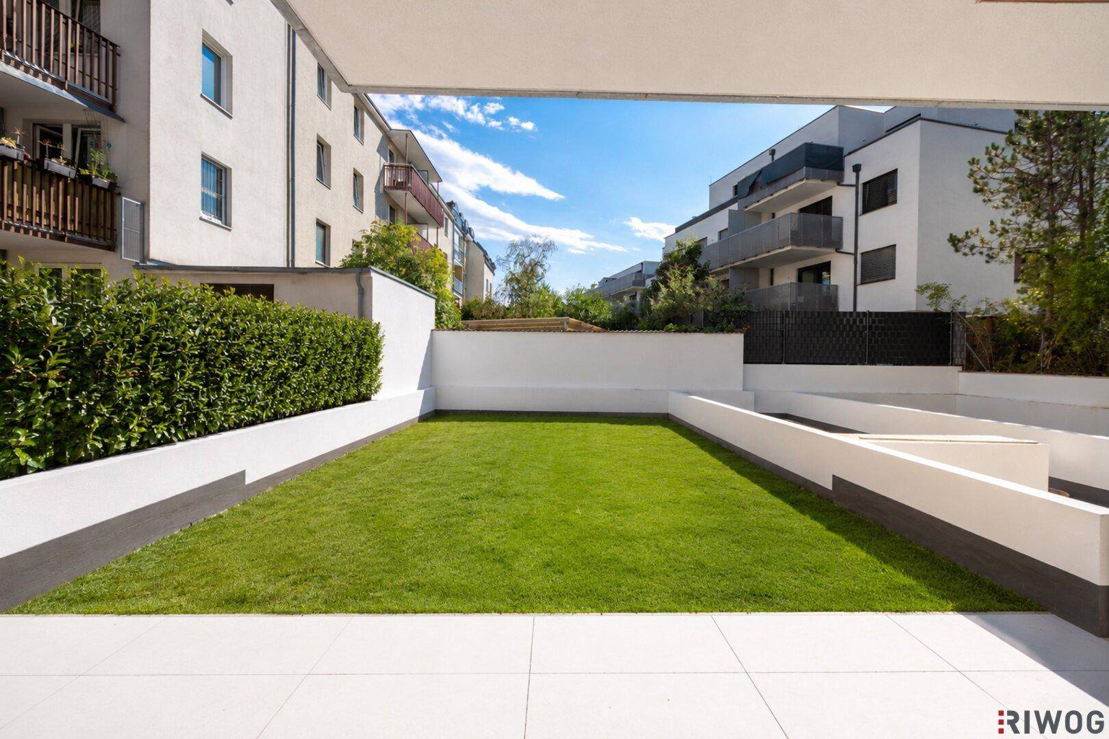 Gepflegter privater Gartenbereich mit Rasenfläche und modernen weißen Begrenzungsmauern zwischen Gebäuden.