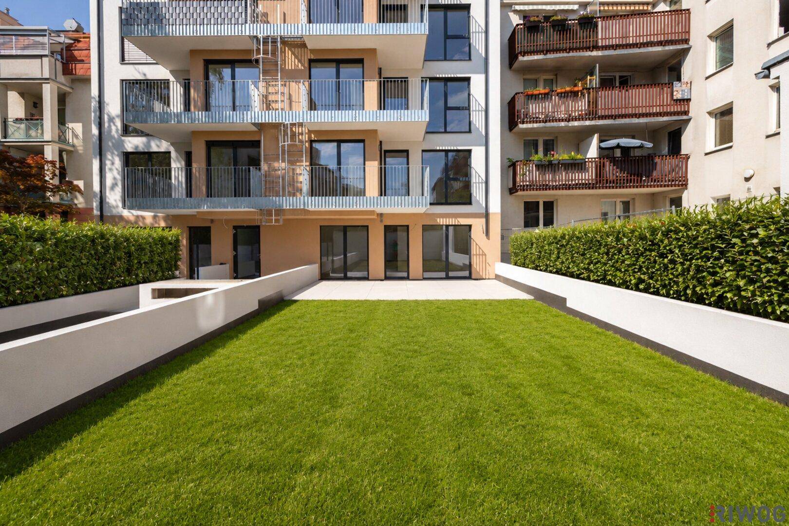 Außenansicht eines modernen Apartmentgebäudes mit mehreren Balkonen und einem gepflegten Gartenbereich im Erdgeschoss.