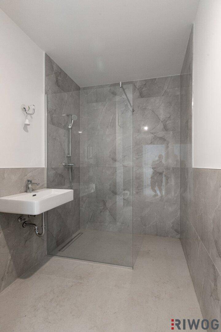 Modernes Badezimmer mit grauen Fliesen, einer begehbaren Dusche und einem schwebenden Waschbecken.