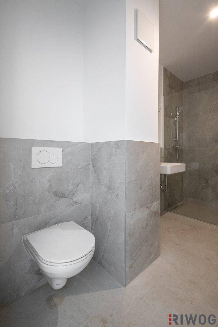 Modernes Badezimmer mit wandhängender Toilette und eleganten grauen Fliesen, die ein zeitgemäßes Design schaffen.