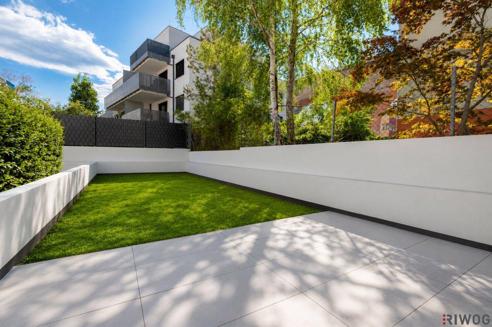 Gepflegter Gartenbereich mit Rasenfläche und gepflasterter Terrasse im Freien.