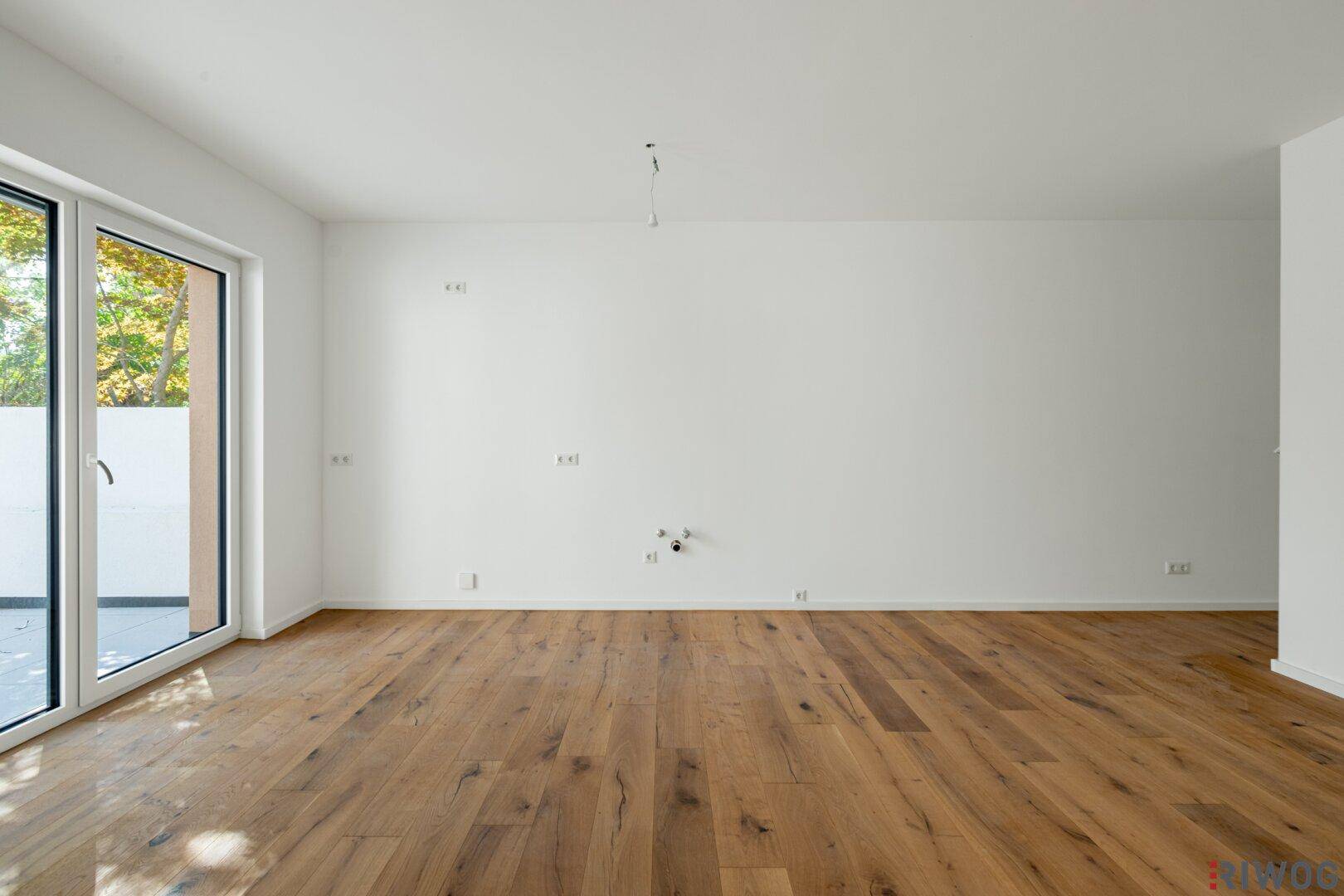 Geräumiger, unmöblierter Wohnbereich mit Holzboden und Zugang zur Terrasse.