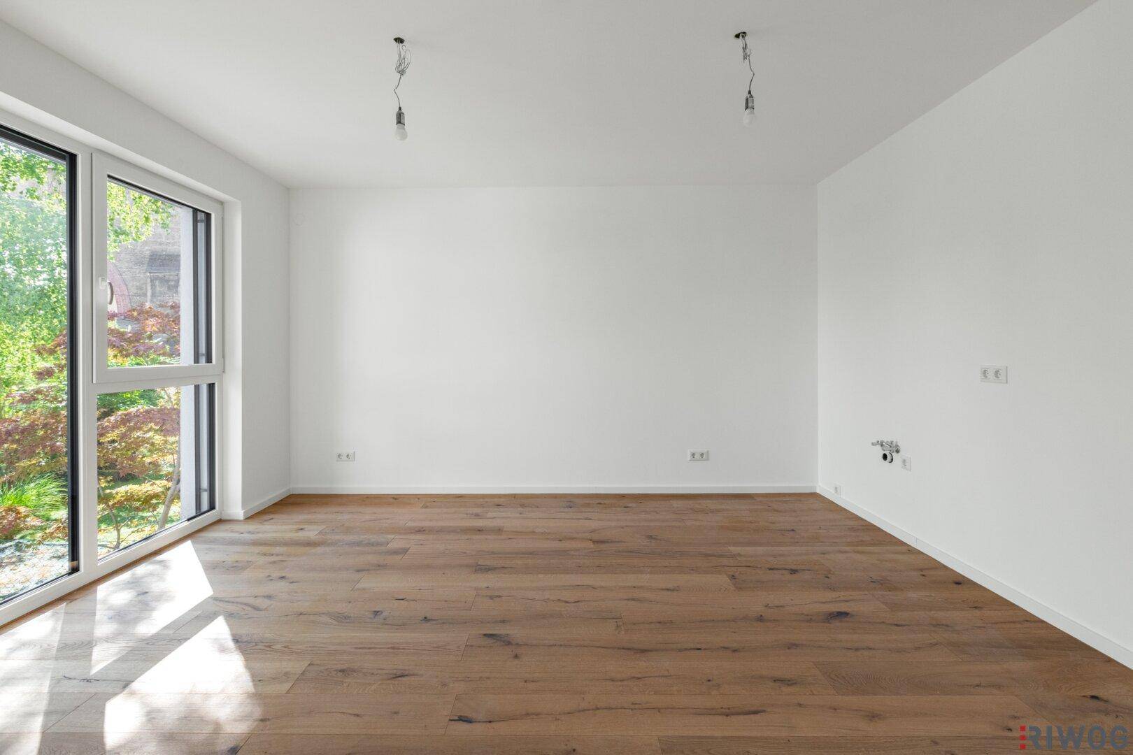 Heller, leerer Raum mit Holzboden und großen Fenstern, die viel Tageslicht hereinlassen.