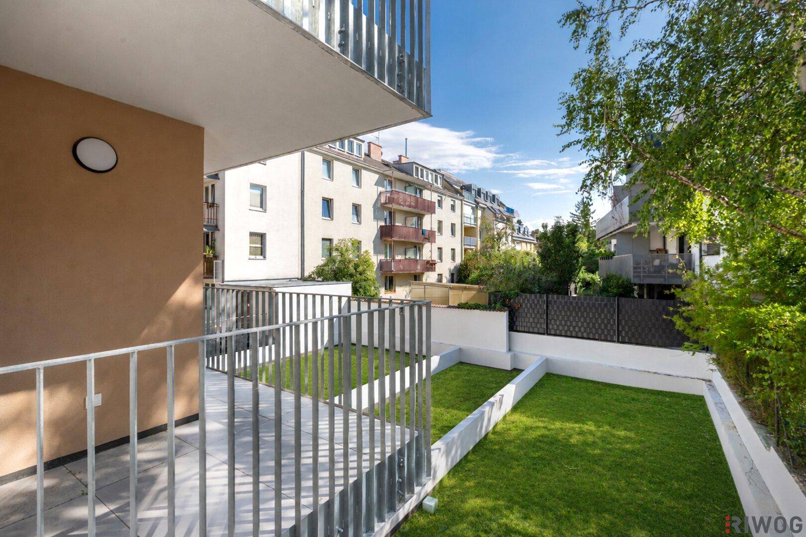 Balkon mit Blick auf einen kleinen privaten Gartenbereich und die umliegenden Gebäude.