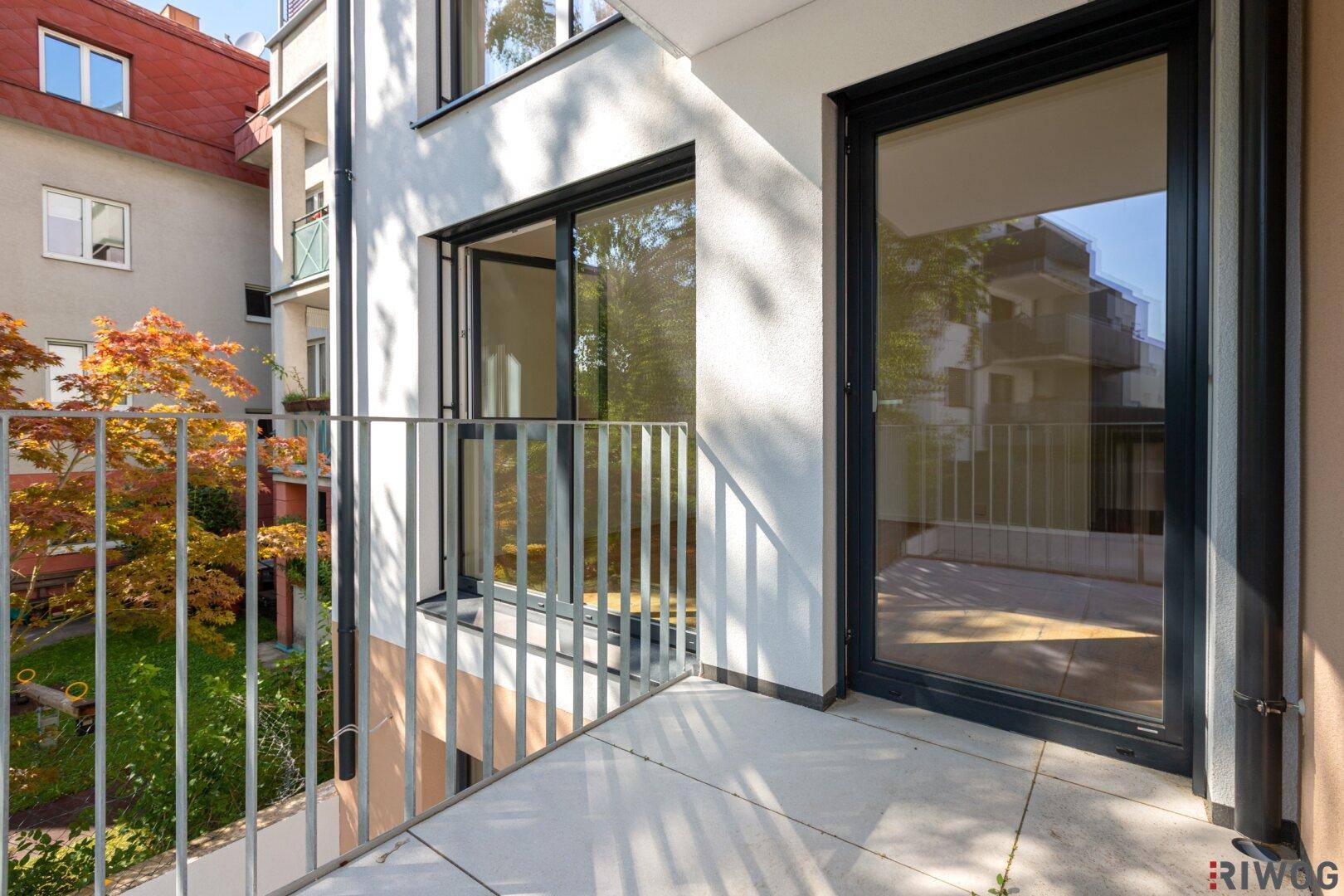 Heller Balkon mit Blick auf grüne Bäume und die moderne Architektur des Nachbargebäudes.