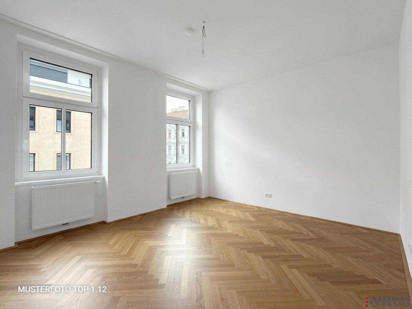 Lichtdurchflutetes, leeres Zimmer mit zwei Fenstern und klassischem Fischgrätparkett.