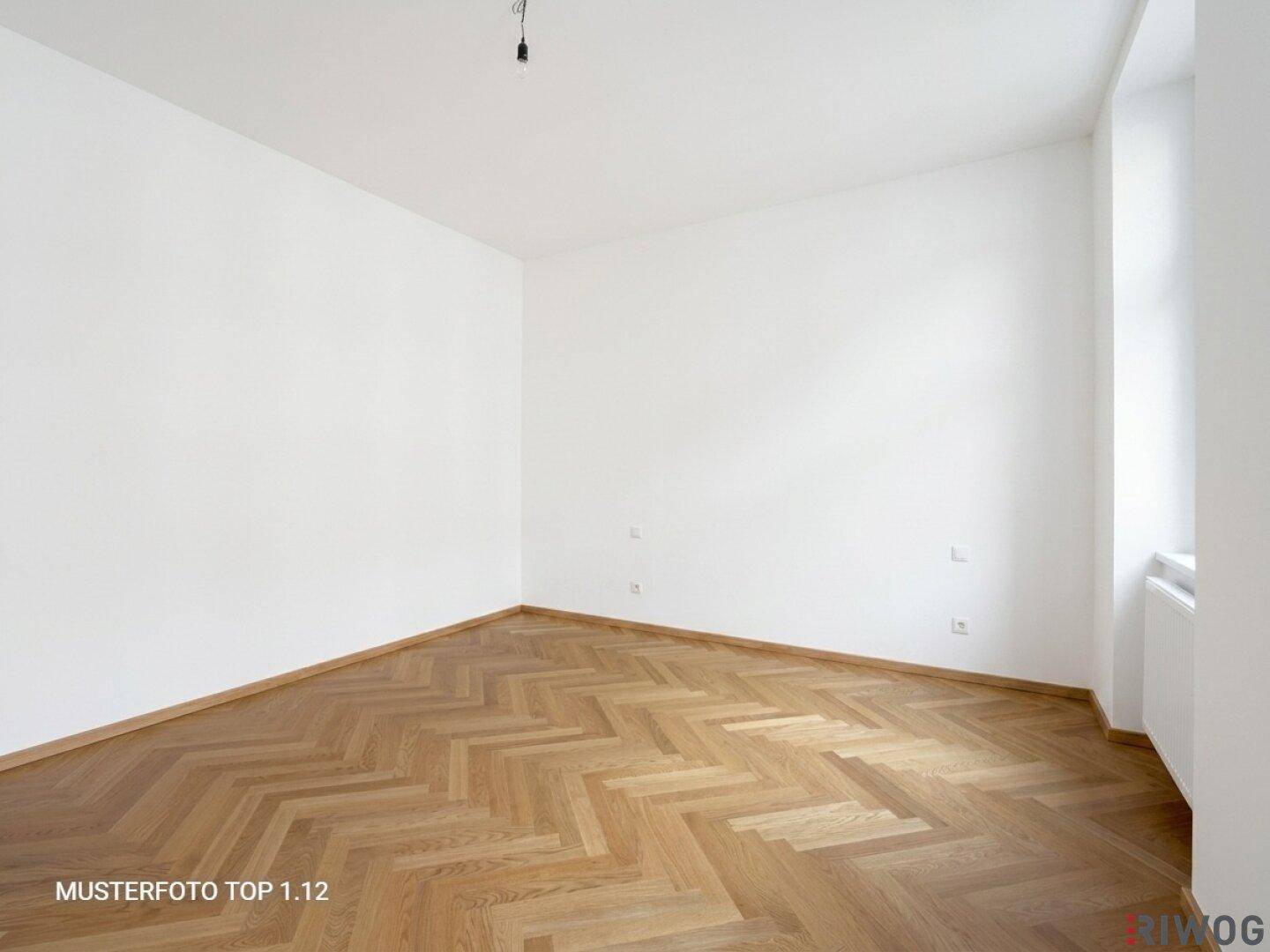 Helles, leeres Zimmer mit weiß gestrichenen Wänden und elegantem Fischgrätparkett.