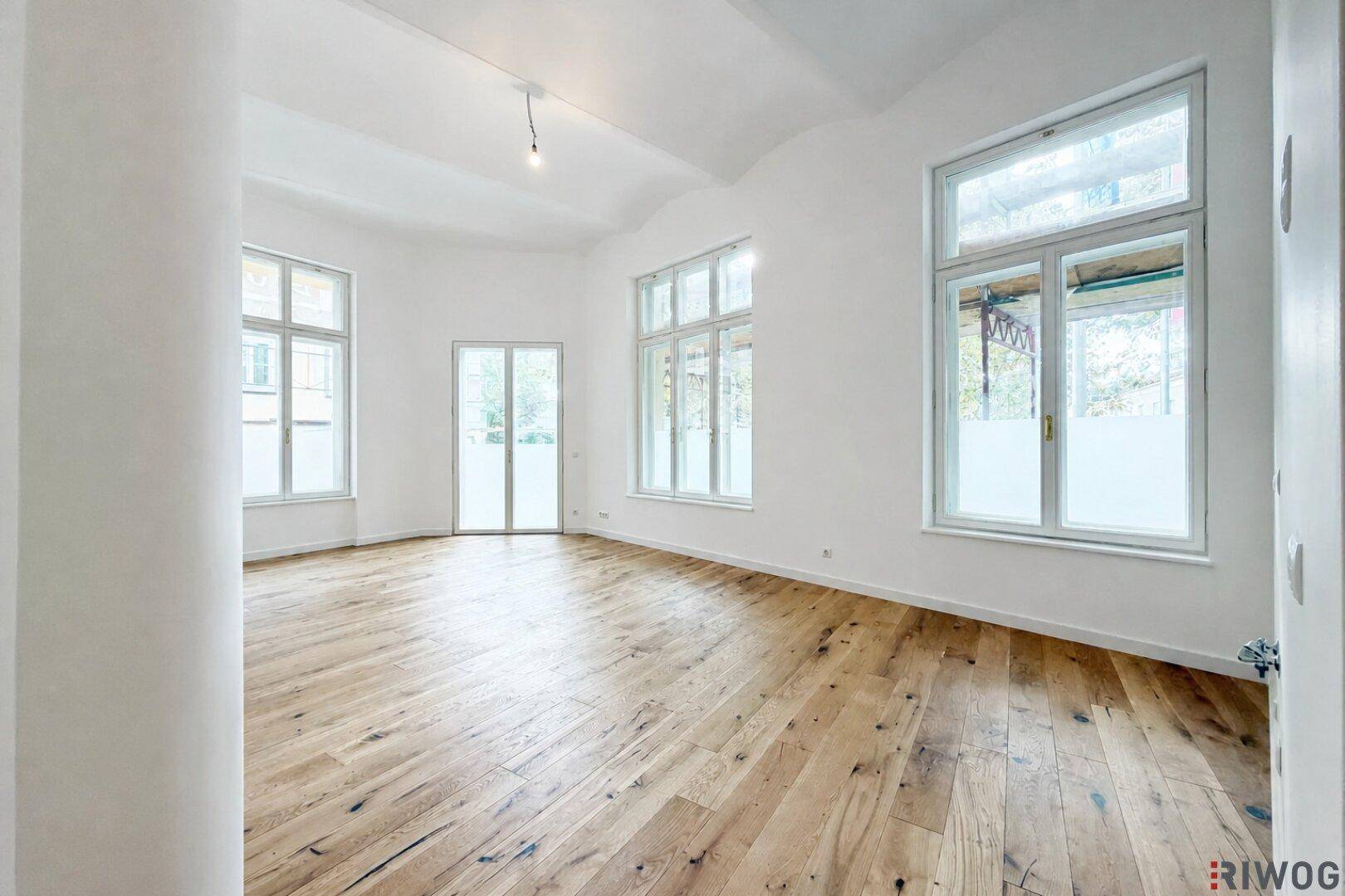 Geräumiger, heller Raum mit hohen Decken, großen Fenstern und elegantem Holzboden, bereit zur Einrichtung.