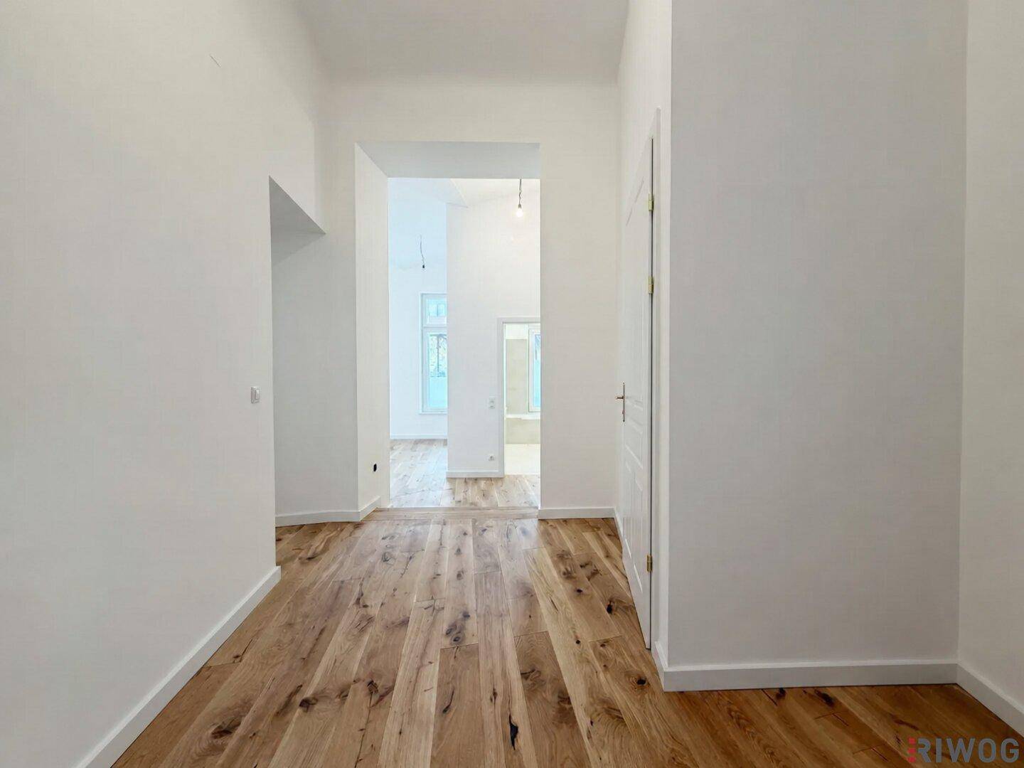 Langer, heller Flur mit hohen Decken und Holzboden, der eine offene Raumgestaltung andeutet.