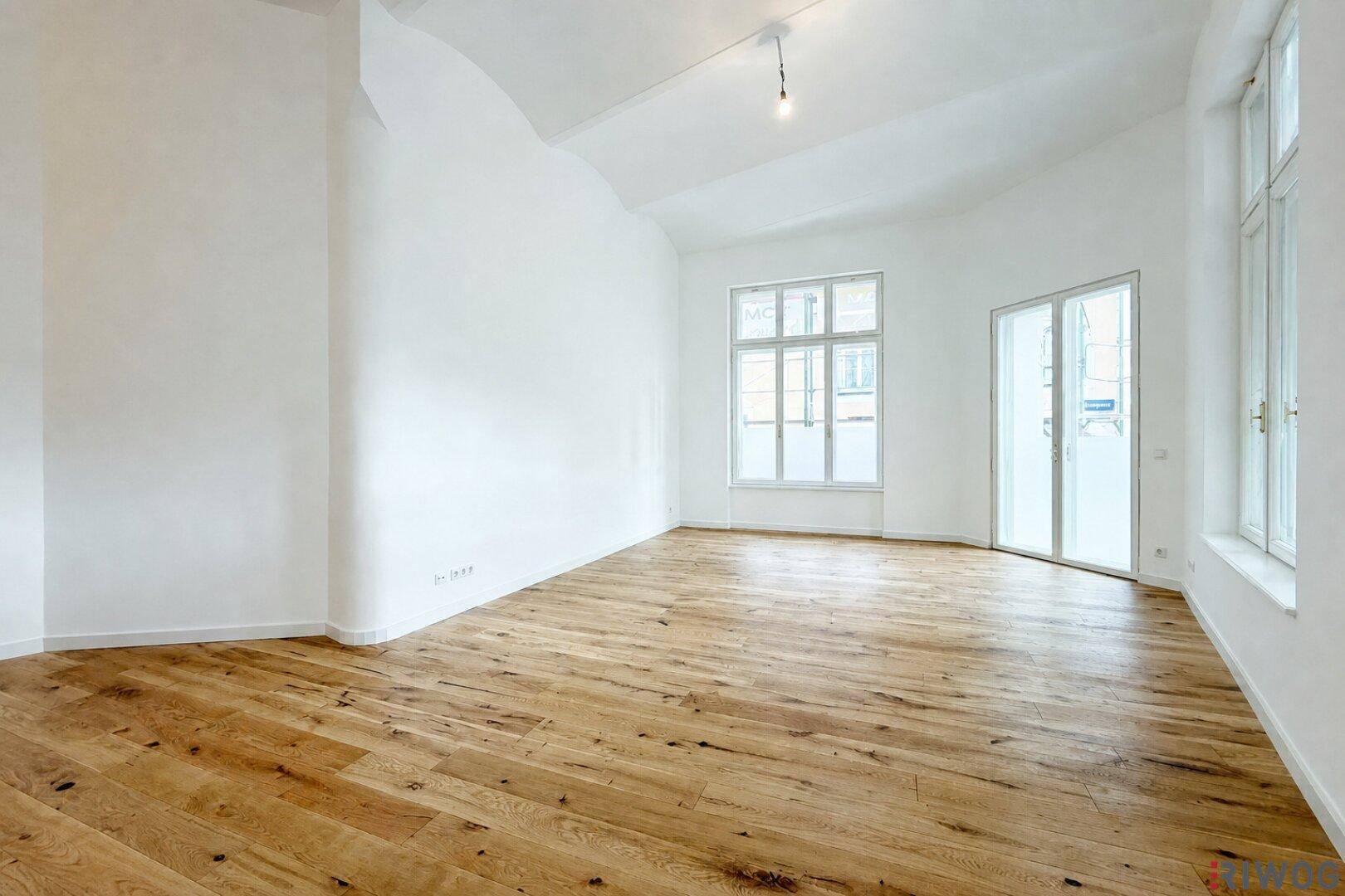Lichtdurchfluteter, leerer Raum mit hohen Decken und Holzboden, ideal für individuelle Gestaltungsmöglichkeiten.