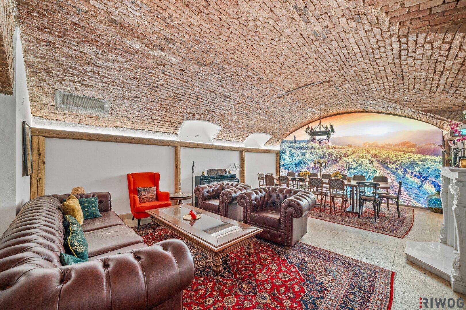Gemütlicher Kellerbereich mit Ziegelgewölbedecke, Ledersofas und einem Wandbild mit Weinbergen.