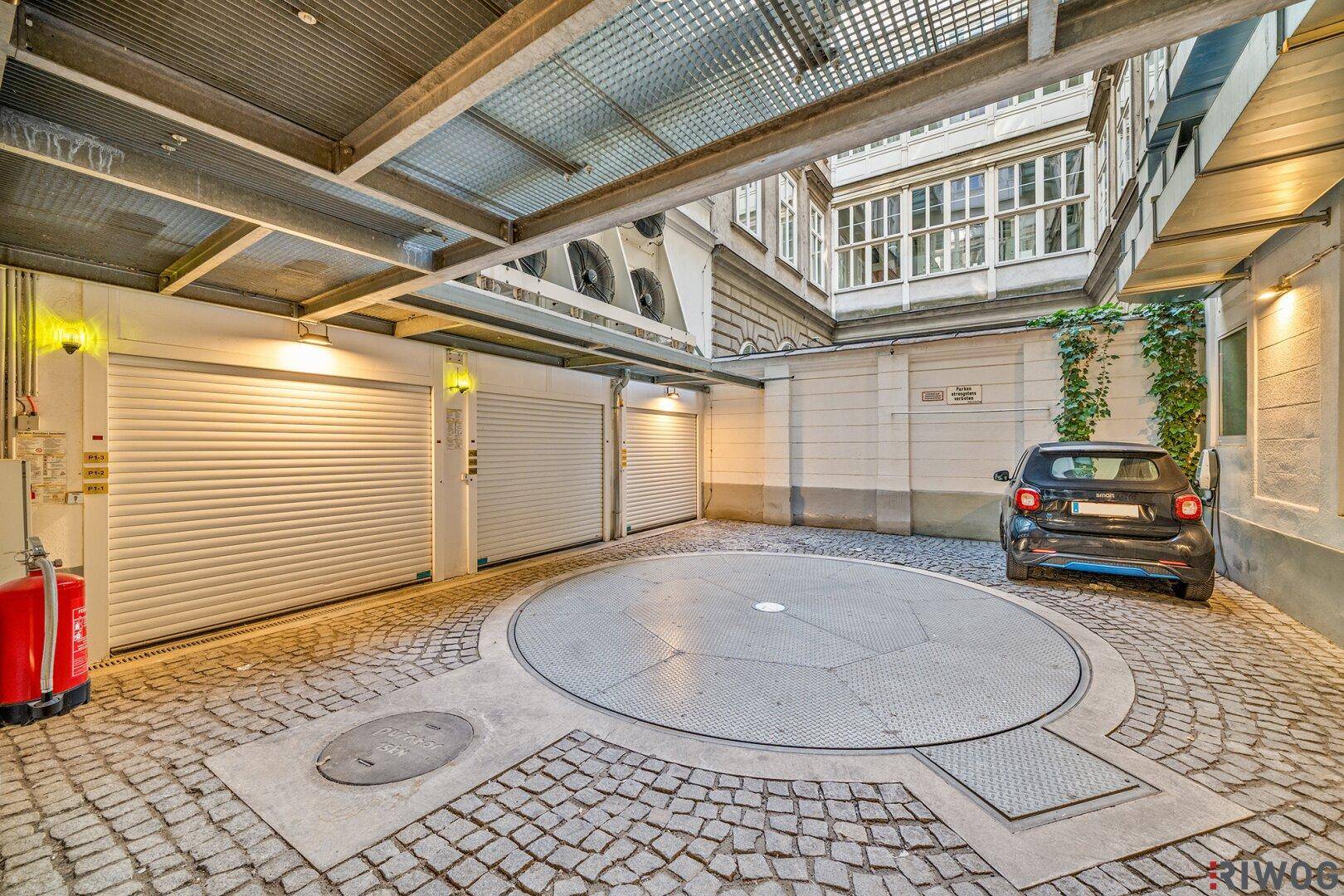 Innenhof-Parkplatz mit Autodrehbühne, Garagentoren und Kopfsteinpflaster.