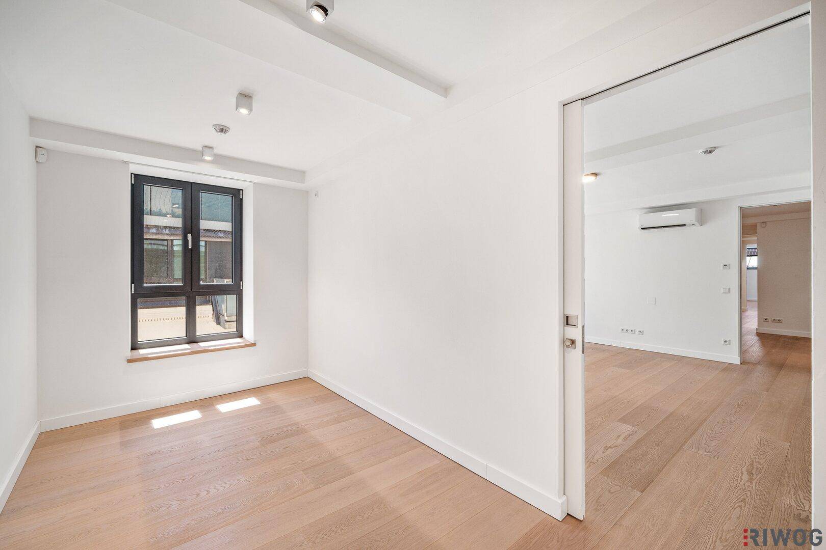 Ruhiges Zimmer mit hellem Holzboden und einem großen Fenster für natürliches Licht.