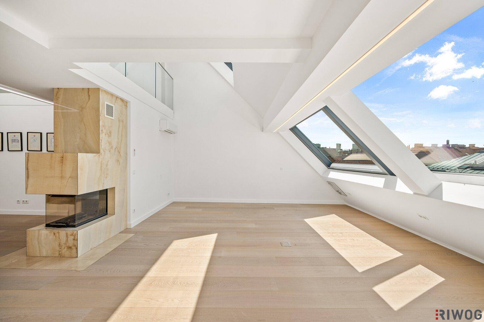 Lichtdurchfluteter Wohnbereich mit Holzboden, modernem Kamin und schrägen Dachfenstern.