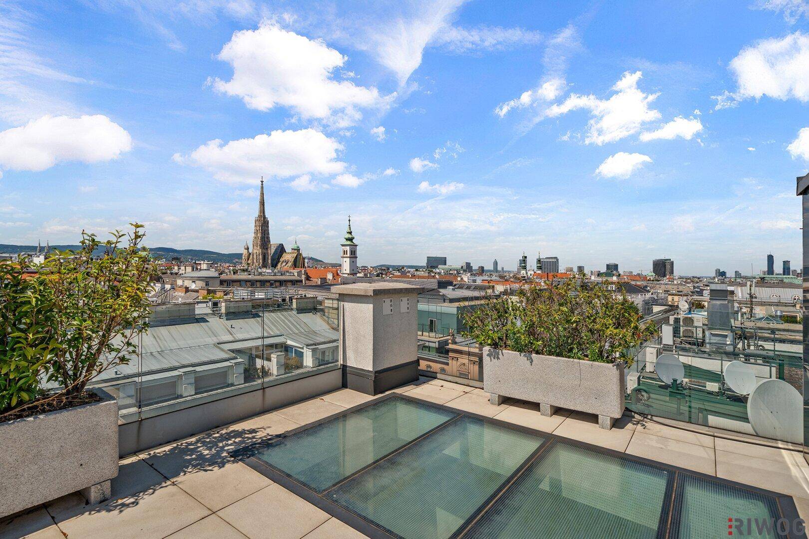 Dachterrasse mit Fliesenboden, Pflanzen und weitem Blick über die Stadt und Kirchtürme.