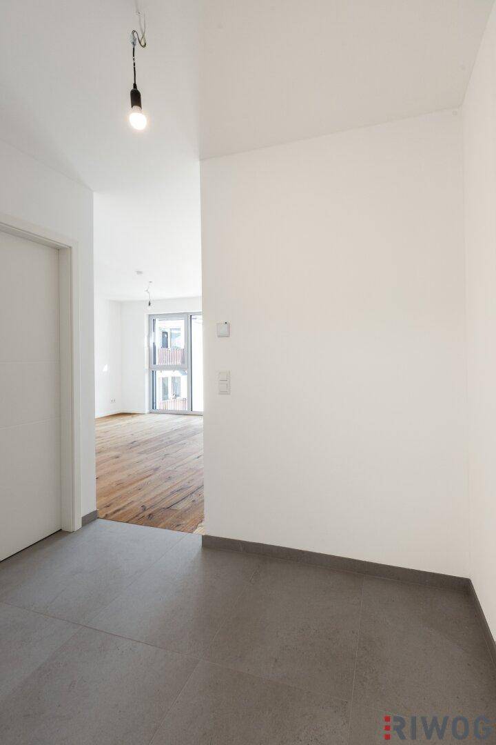 Heller Eingangsbereich mit Fliesenboden, der zu den Wohnräumen mit Holzboden führt.