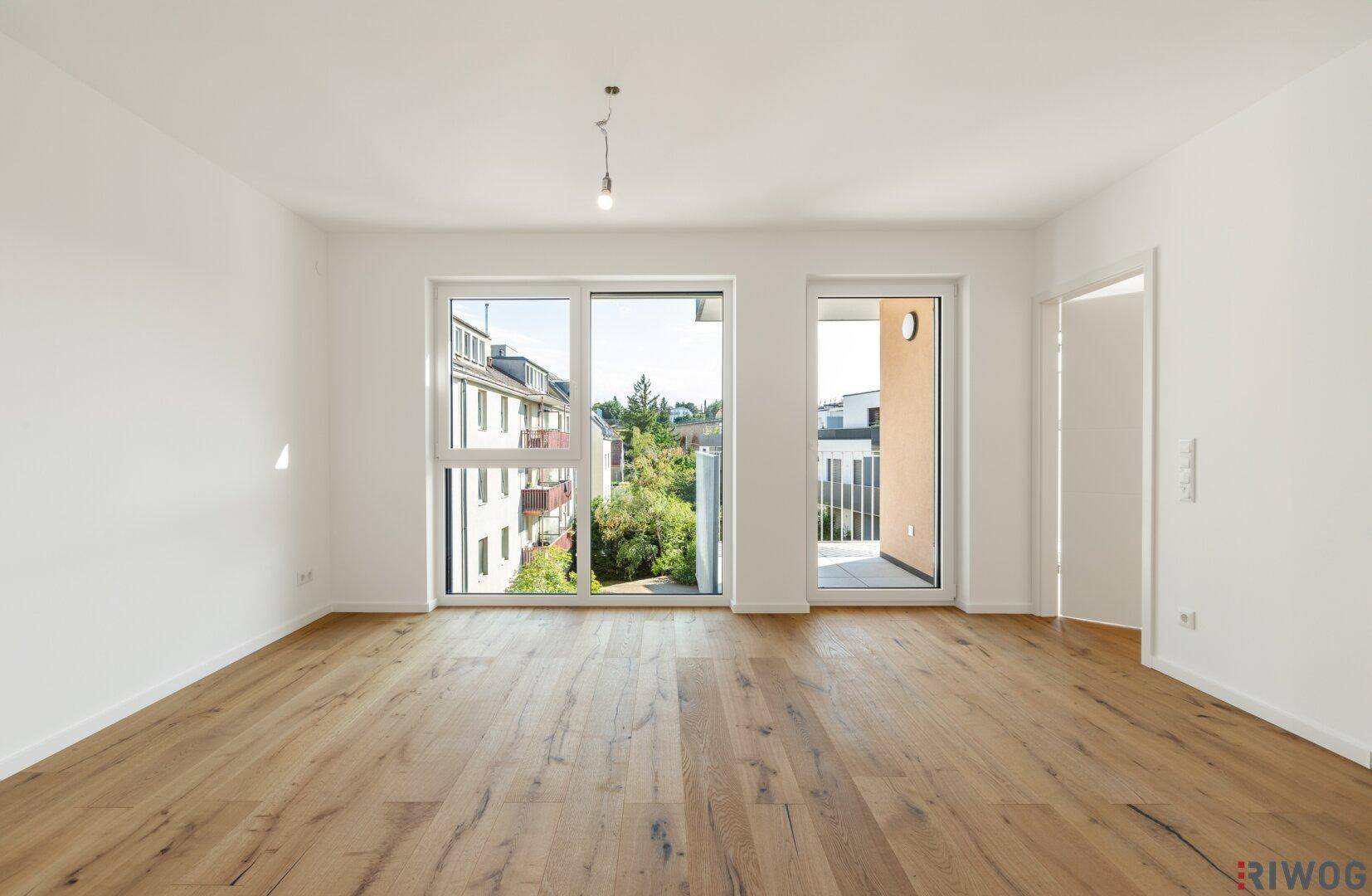 Geräumiger, unmöblierter Wohnbereich mit Holzboden und Zugang zum Balkon.