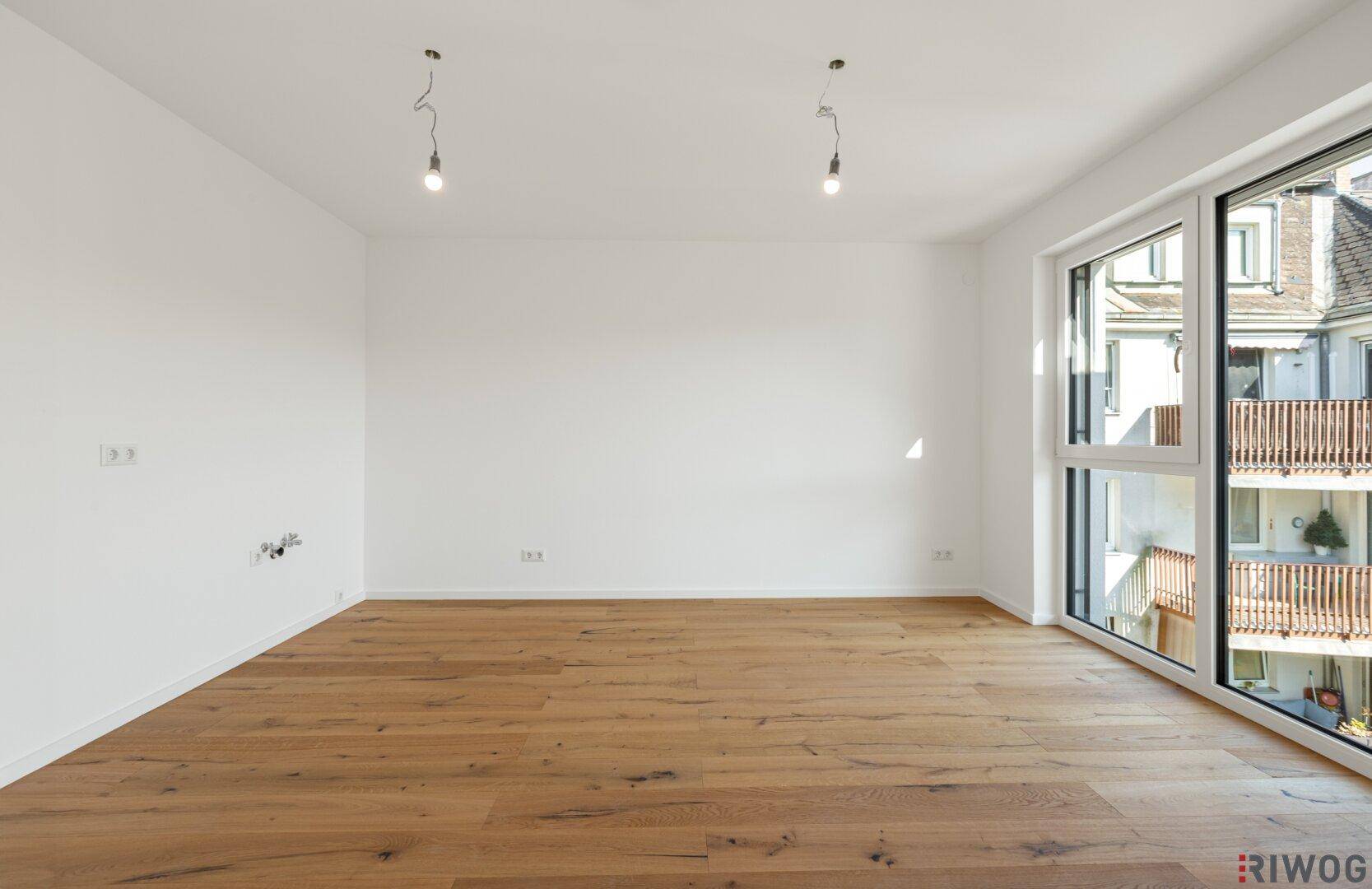 Heller, leerer Wohnraum mit großen Fenstern und Holzboden, bereit zur individuellen Gestaltung.