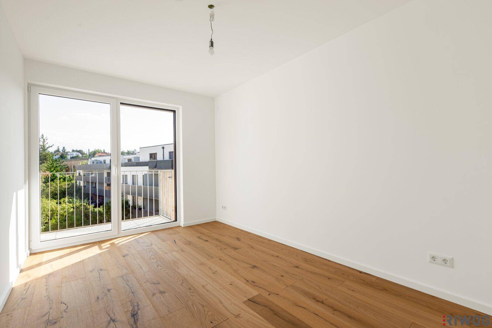Helles, leeres Schlafzimmer mit Holzboden und Zugang zu einem kleinen Balkon.
